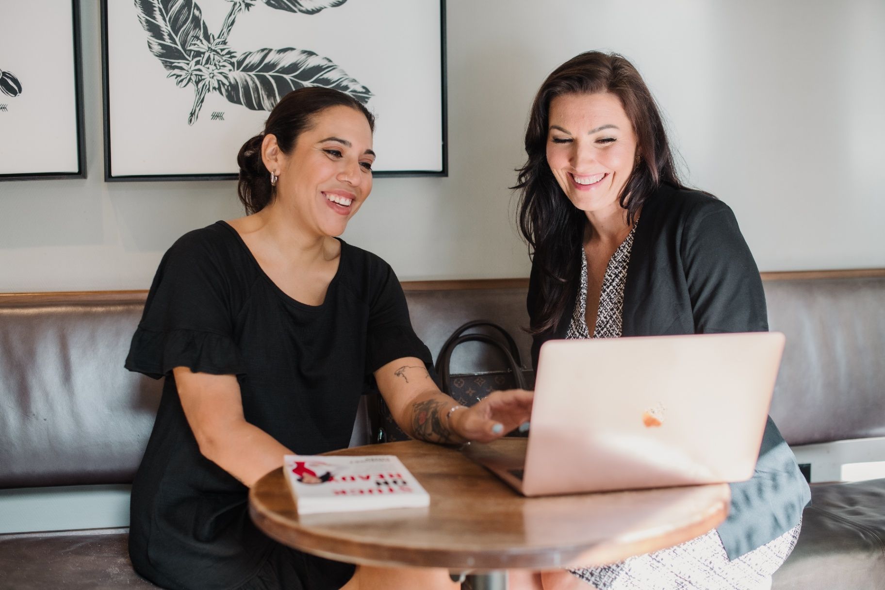 Bridget Hom and a client smiling together as they work on a laptop at a café table